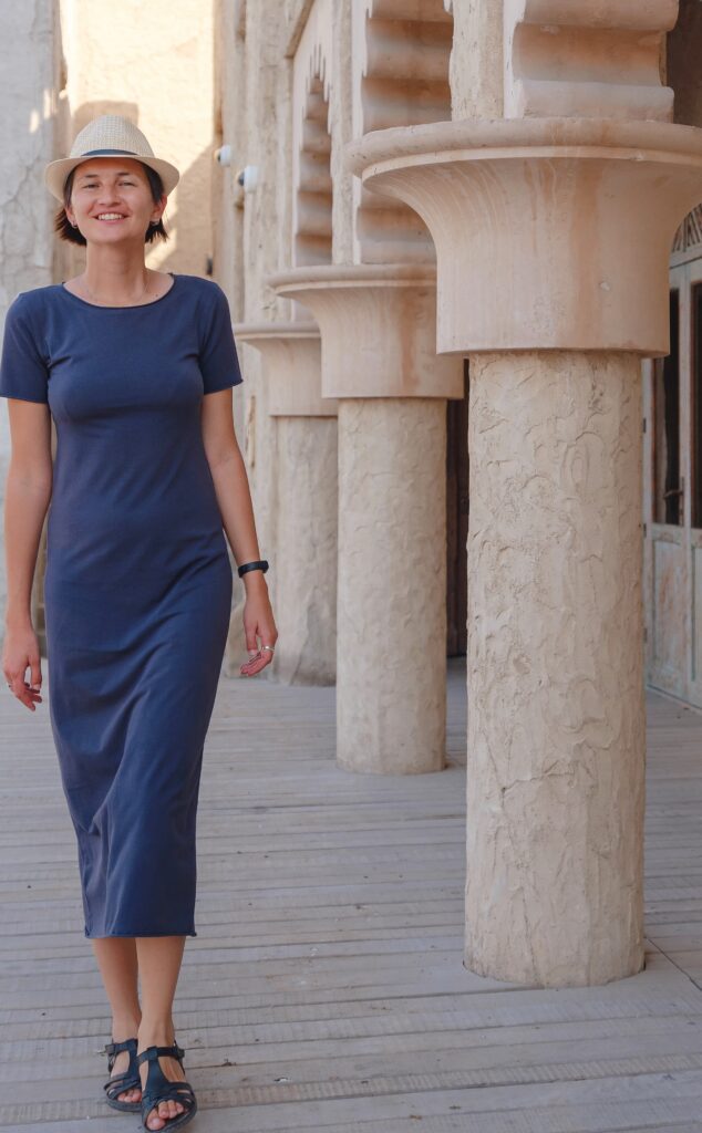 A woman in blue dress walking on sidewalk near pillars.